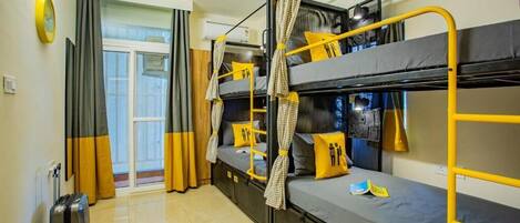 Une chambre de dortoir avec des lits superposés, une valise et une fenêtre avec des rideaux.