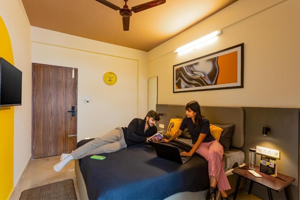 Una habitación de hotel moderna con una cama, un escritorio, una silla, un reloj y un cuadro en la pared.