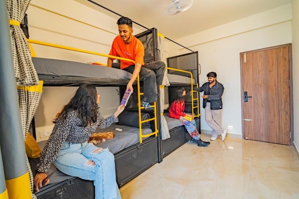 A dormitory room with bunk beds, a wooden door, and a fan on the ceiling.