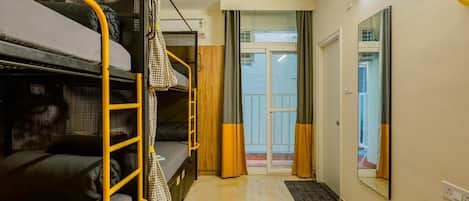 A dormitory room with bunk beds, a small desk, and a window with curtains.