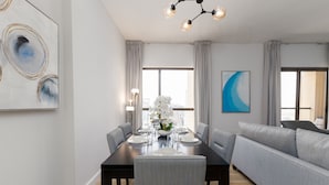A modern dining area with a dark wooden table set for four, surrounded by grey upholstered chairs. A grey sofa is positioned to the right, and a large window provides natural light. - Trendy JBR 2BR w Pool and Gym Marina Views (Dubai)