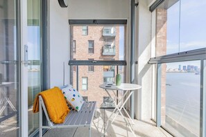 A balcony with a white metal bench, a small round table, and a view of a river and buildings. - Gorgeous 1BD Flat with Incredible Views of the O2 (Greater London)