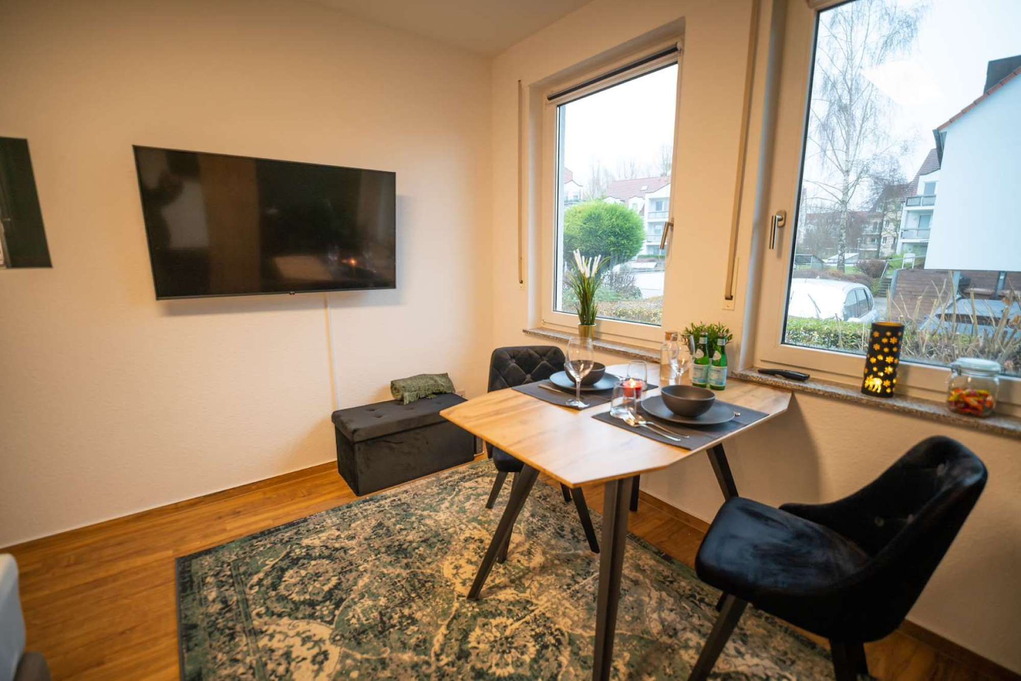 A dining area with a table, chairs, a flat-screen TV, and a window with a view of the outside.