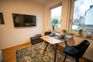 A dining area with a table, chairs, a flat-screen TV, and a window with a view of the outside. - RR | Cozy Apartment | Parking | Kitchen | WIFI (Magdeburg)