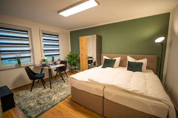 A hotel room with a bed, bedside table, desk, chair, and a view through the window.
