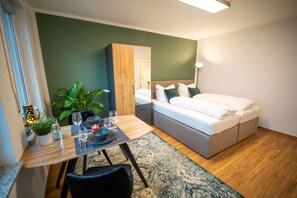 Un dormitorio compacto con cama, mesita de noche y un pequeño comedor con mesa y sillas.