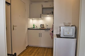 A narrow kitchen with white cabinets, a wooden floor, a kettle, a coffee maker, and a microwave on a small table. - RR | Tiny Apartment | Parking | Kitchen | WIFI (Magdeburg)
