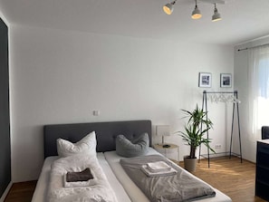 Une chambre moderne avec un grand lit, des tables de chevet, une plante et un bureau avec une chaise.