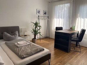 A hotel room with a bed, desk, chair, potted plant, and two framed pictures on the wall. - RR | Tiny Apartment | Parking | Kitchen | WIFI (Magdeburg)
