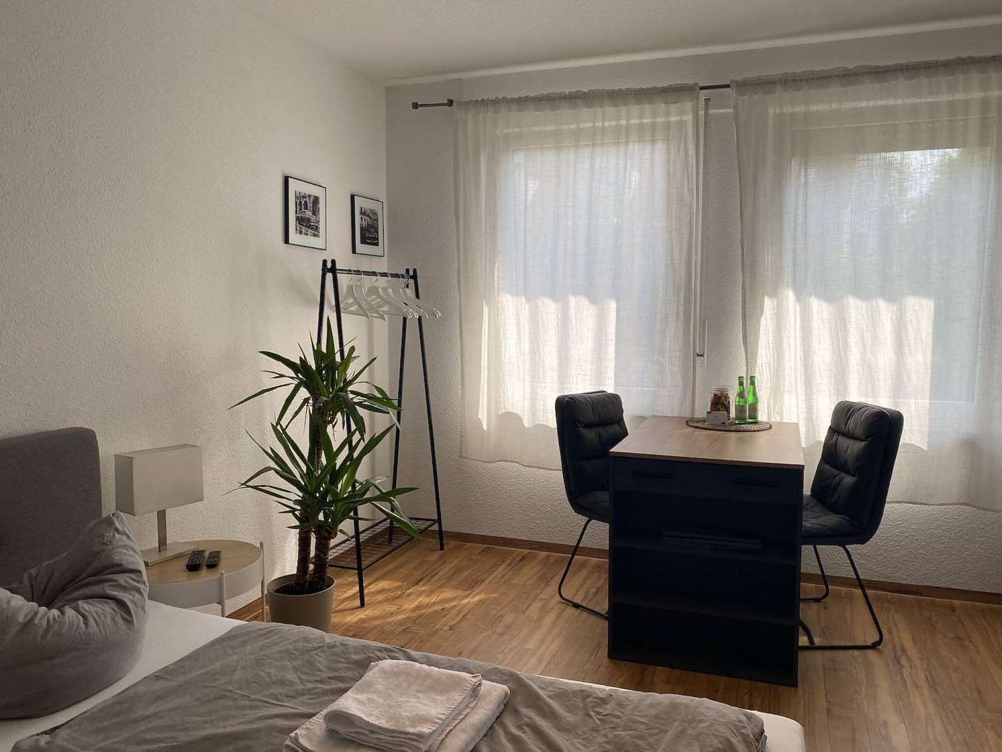 A hotel room with a bed, a desk, a chair, a potted plant, and a window with curtains.