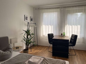 A hotel room with a bed, a desk, a chair, a potted plant, and a window with curtains. - RR | Tiny Apartment | Parking | Kitchen | WIFI (Magdeburg)