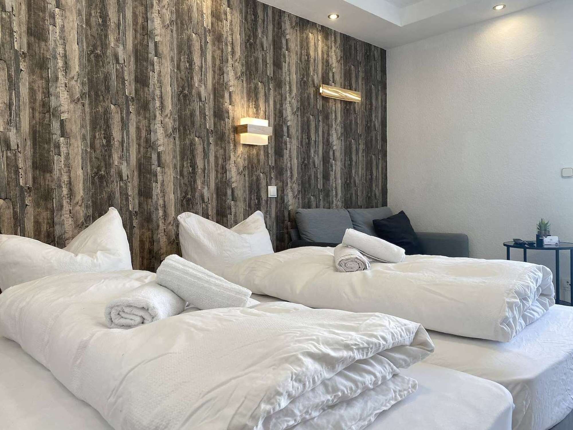 A hotel room with two beds, a wooden accent wall, and a small bedside table with a lamp.