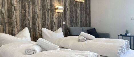 A hotel room with two beds, a wooden accent wall, and a small bedside table with a lamp.