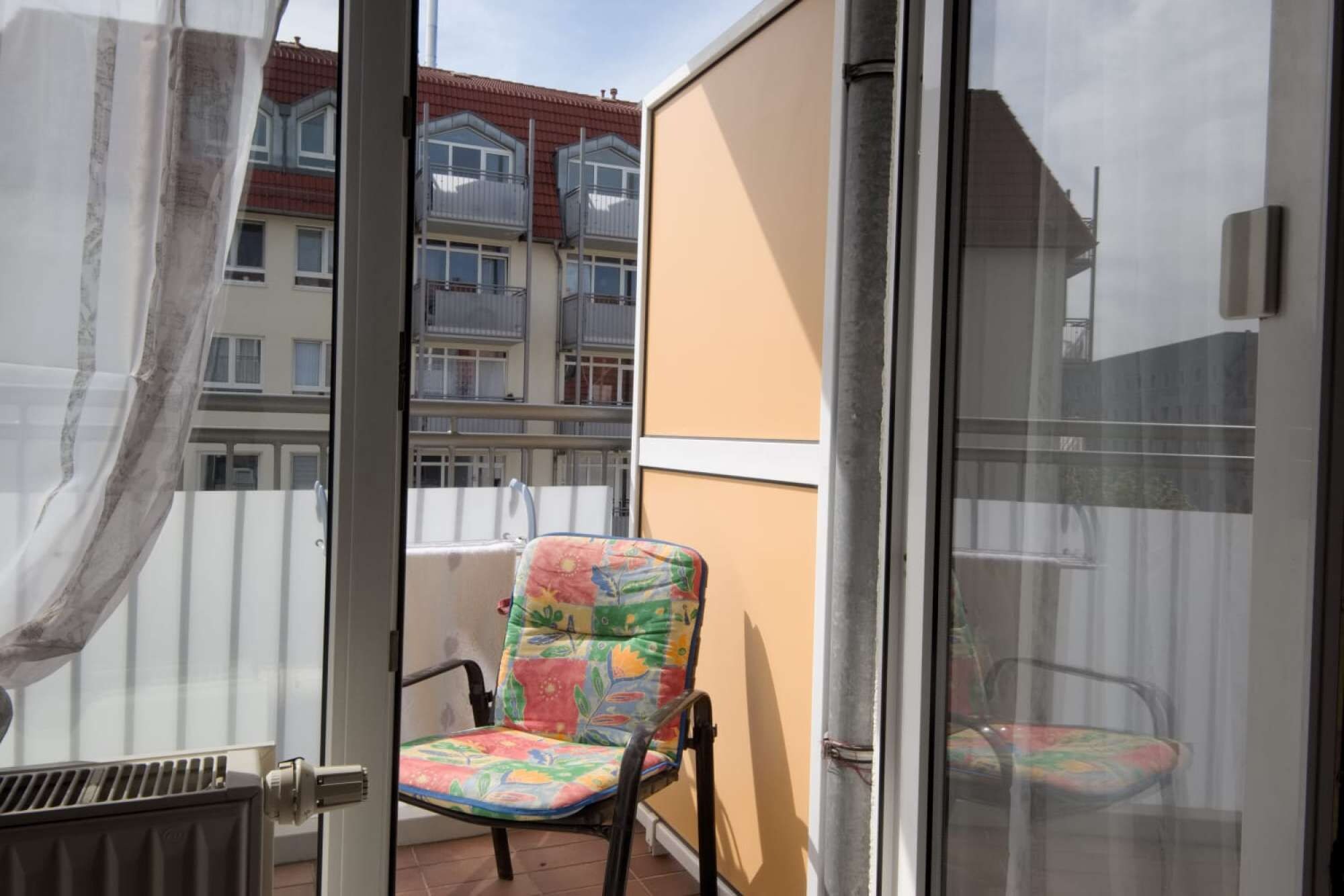 Un balcon avec une chaise, un radiateur et une vue sur un immeuble doté de balcons.