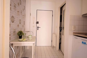 A narrow hallway with a white door, a small table with a potted plant, and a tiled floor. - RR | Charming Apartment - Balcony - WIFI - Kitchen (Magdeburg)
