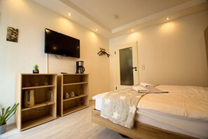A hotel room with a bed, a television, a coffee machine, and a shelf with various items. - RR | Charming Apartment - Balcony - WIFI - Kitchen (Magdeburg)