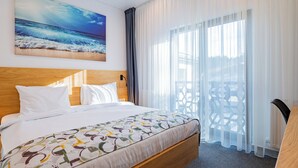 A hotel room with a large bed, a wooden headboard, a painting of the ocean, sheer curtains, and a view of the outdoors. - Q Villa (Sacele)