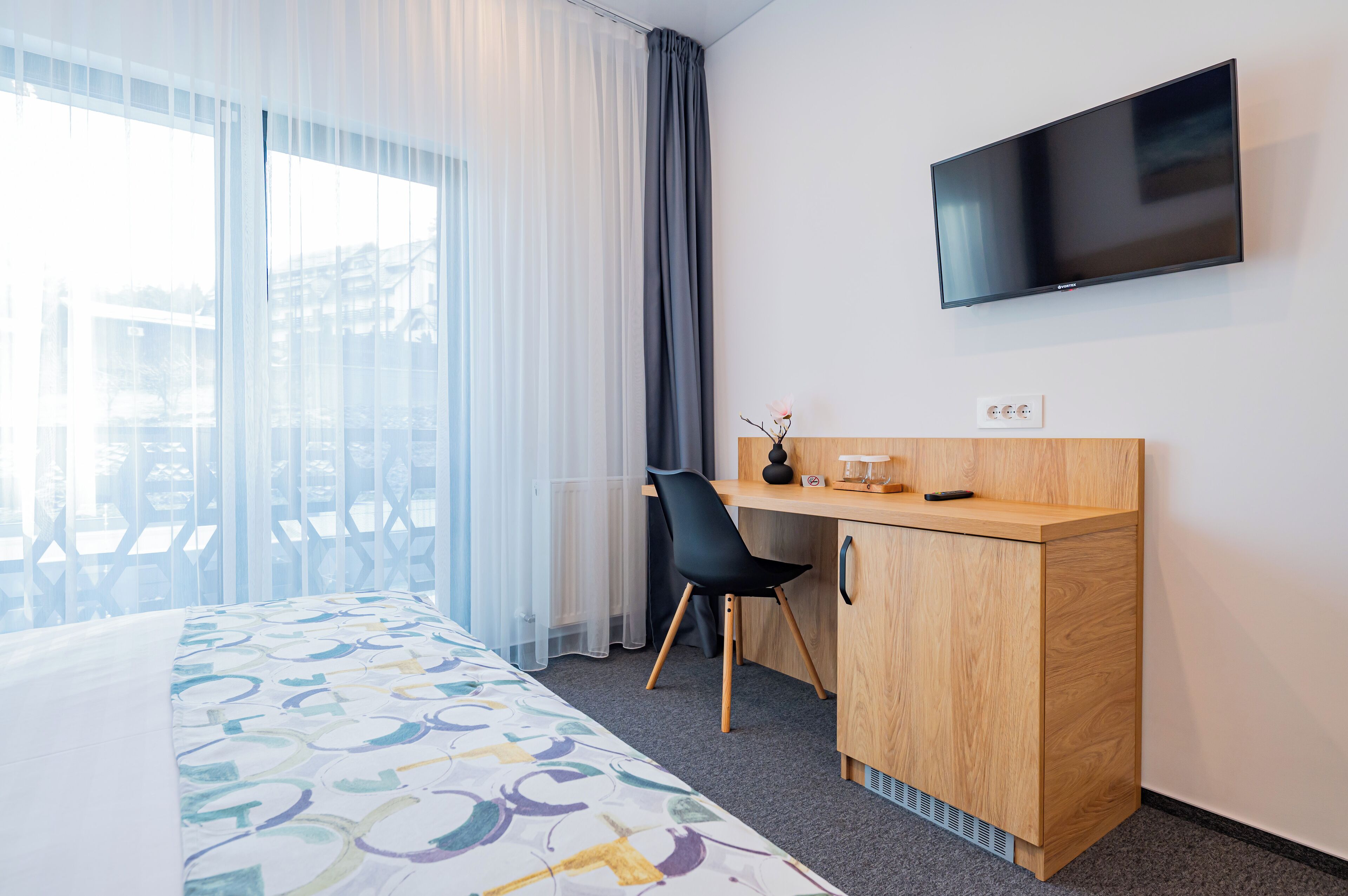 Une chambre d’hôtel avec un lit, un bureau, une chaise, une télévision et une fenêtre avec des rideaux.