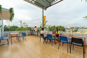 An outdoor seating area with tables and chairs, surrounded by greenery and a view of buildings in the distance. - The Hosteller Bangalore, Koramangala (Karnataka)