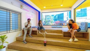 A modern interior with wooden steps, a neon sign, and large windows. - The Hosteller Bangalore, Koramangala (Karnataka)