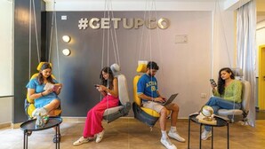 Four people seated on swing chairs in a modern lobby with a '#GETUPGO' sign on the wall. - The Hosteller Bangalore, Koramangala (Karnataka)