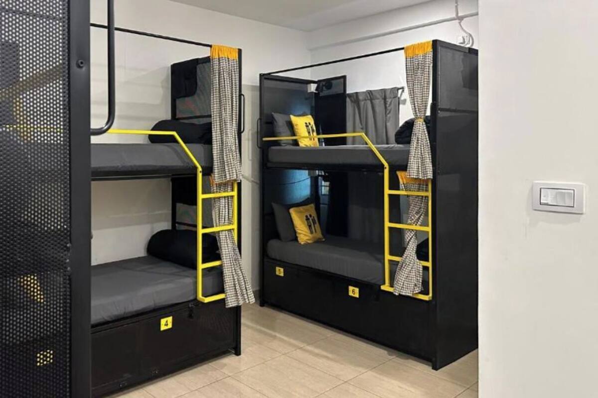 Deux lits superposés dotés de compartiments de rangement, chacun muni d’une échelle jaune et d’un tissu à carreaux suspendu.