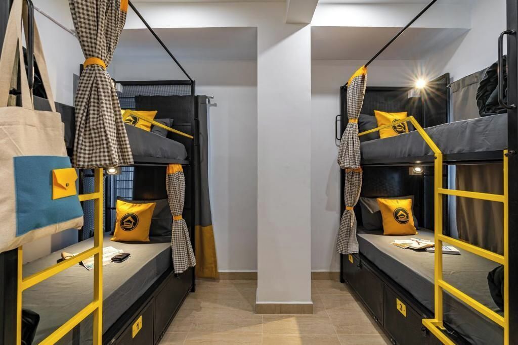 A room with bunk beds, each with a yellow frame and checkered curtains. There are pillows with a yellow logo on the beds.