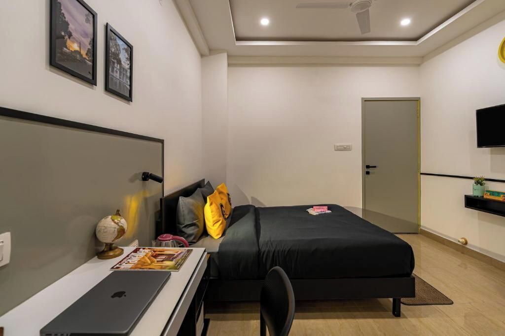A modern bedroom with a bed, desk, laptop, and a TV on the wall.
