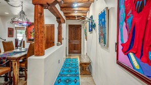A hallway with a wooden ceiling, a blue patterned rug, and a dining area with a table and chairs.