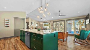 Een moderne keuken met een groen kookeiland, houten vloeren en hanglampen.