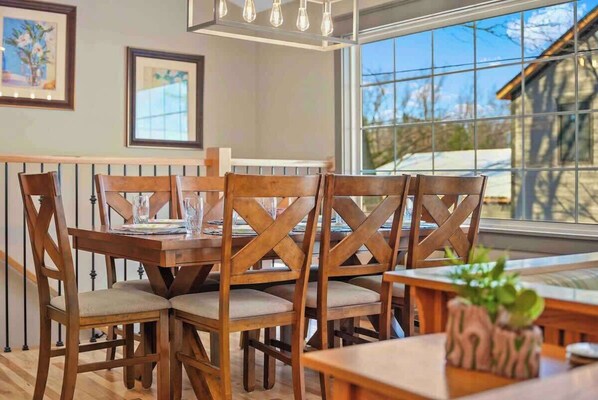 A dining area with wooden chairs and a table, framed pictures on the wall, and a window with a view of the outside. - Grandview (Denton Township)