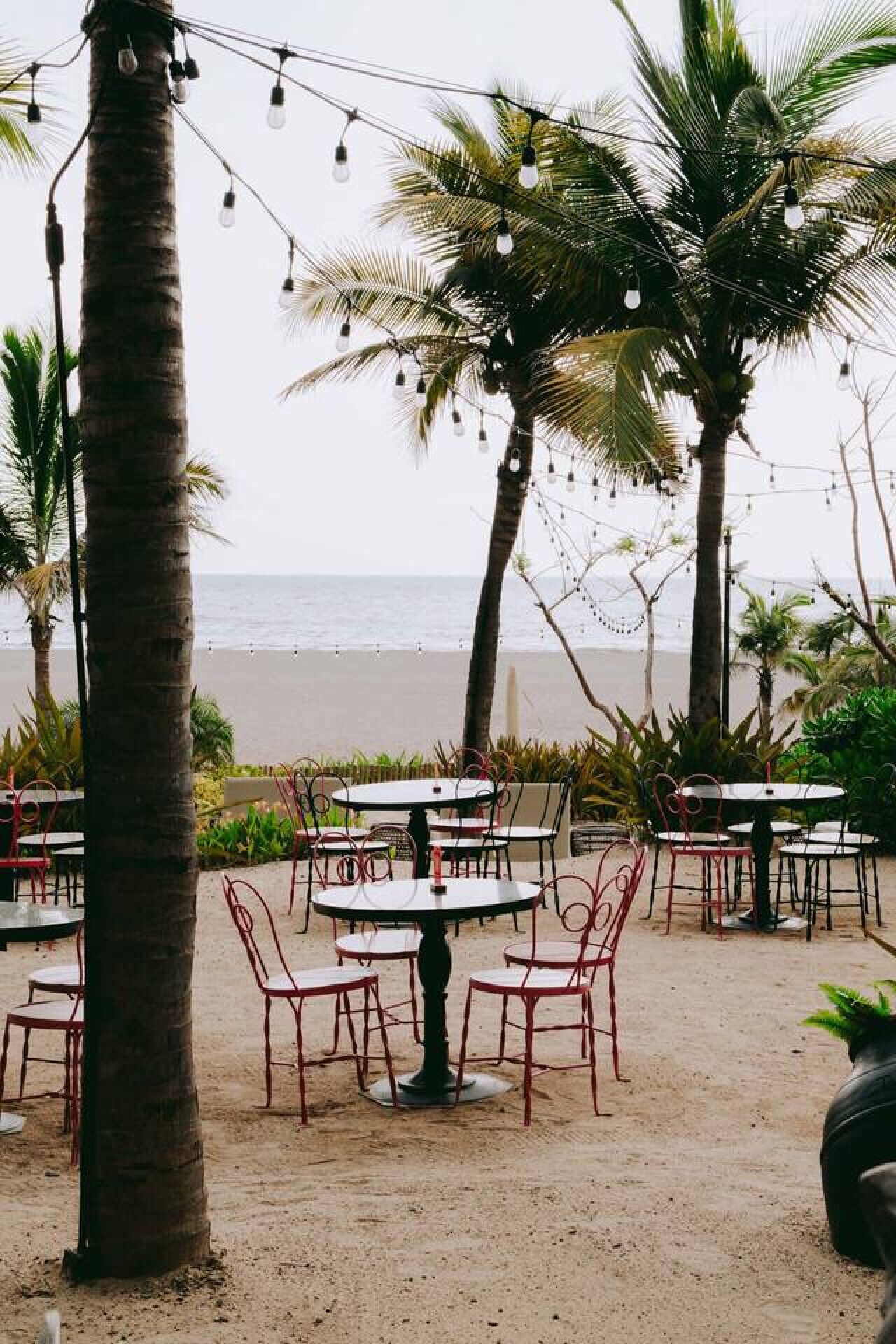 Sitzgelegenheiten im Freien mit Tischen und Stühlen, Palmen und Blick auf den Strand.