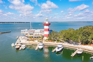 A lighthouse with a red and white striped tower, a dock with several boats, and a building with a covered area.