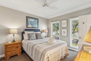 A bedroom with a bed, nightstand, dresser, ceiling fan, and a window with a view.