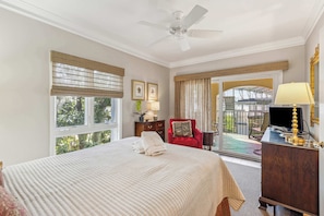 A hotel room with a bed, a desk, a chair, a television, and a balcony with a view of greenery.