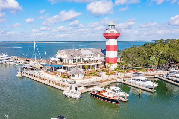 A marina with boats docked, a prominent lighthouse, and a building with a sloped roof.