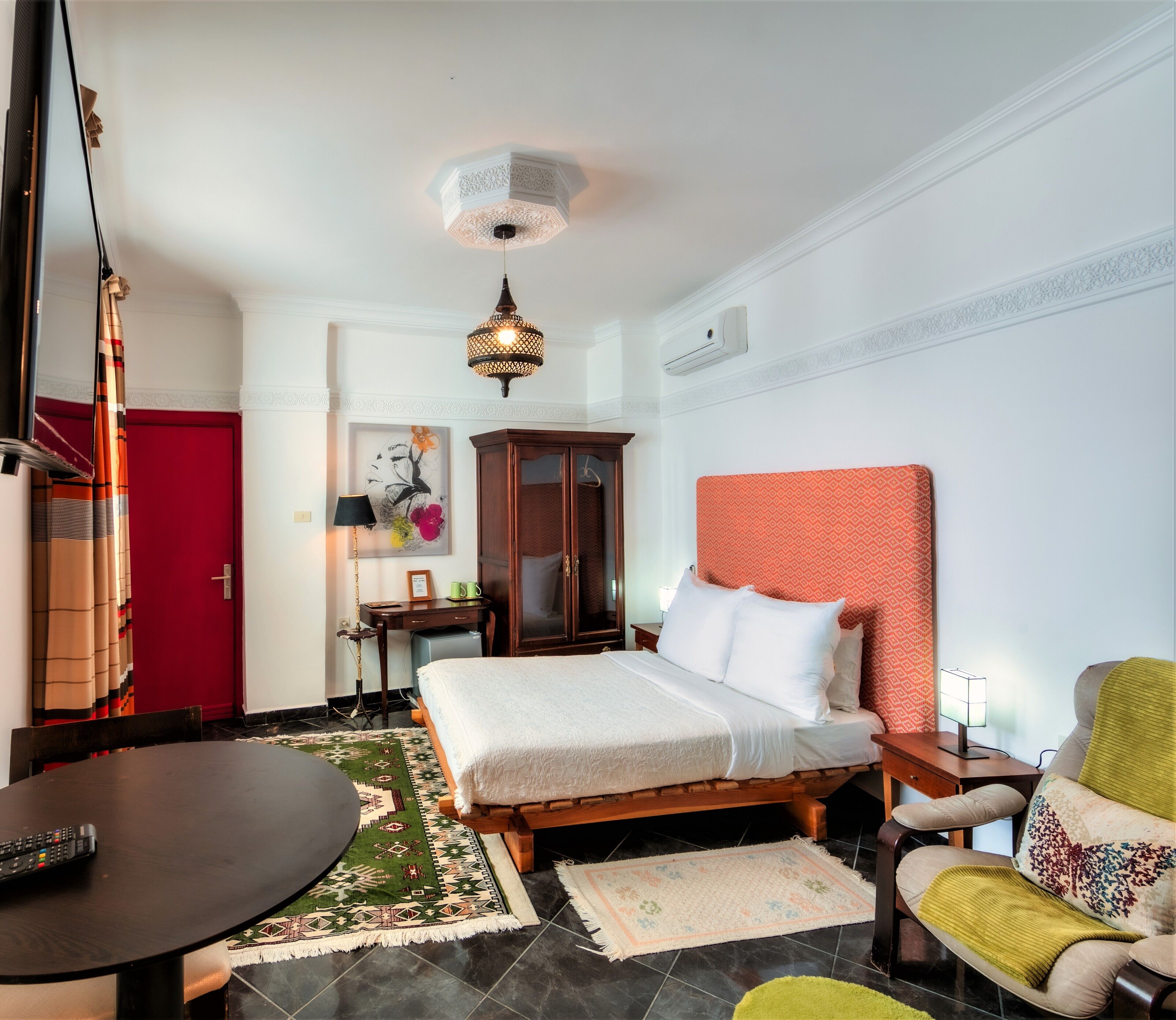 A hotel room with a bed, a desk, a chair, a table, and a red door.