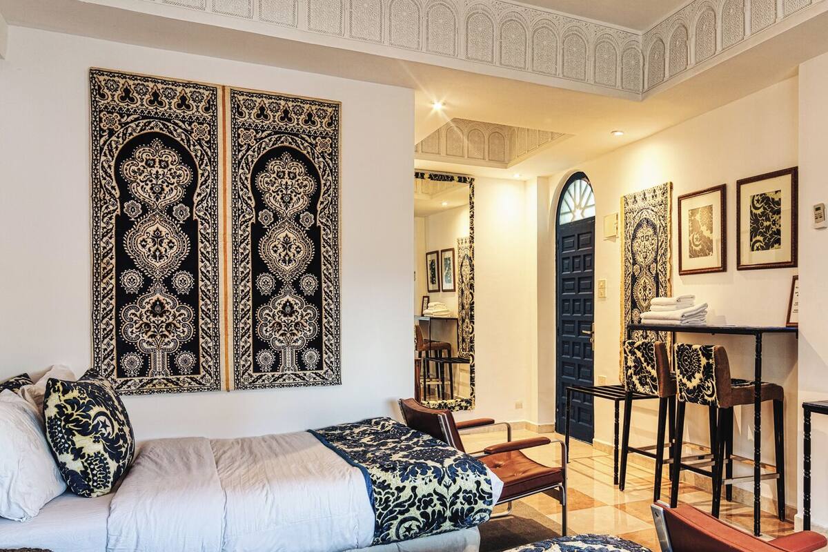 A hotel room with a large bed, a desk, and a chair. There are decorative wall panels and a chandelier.