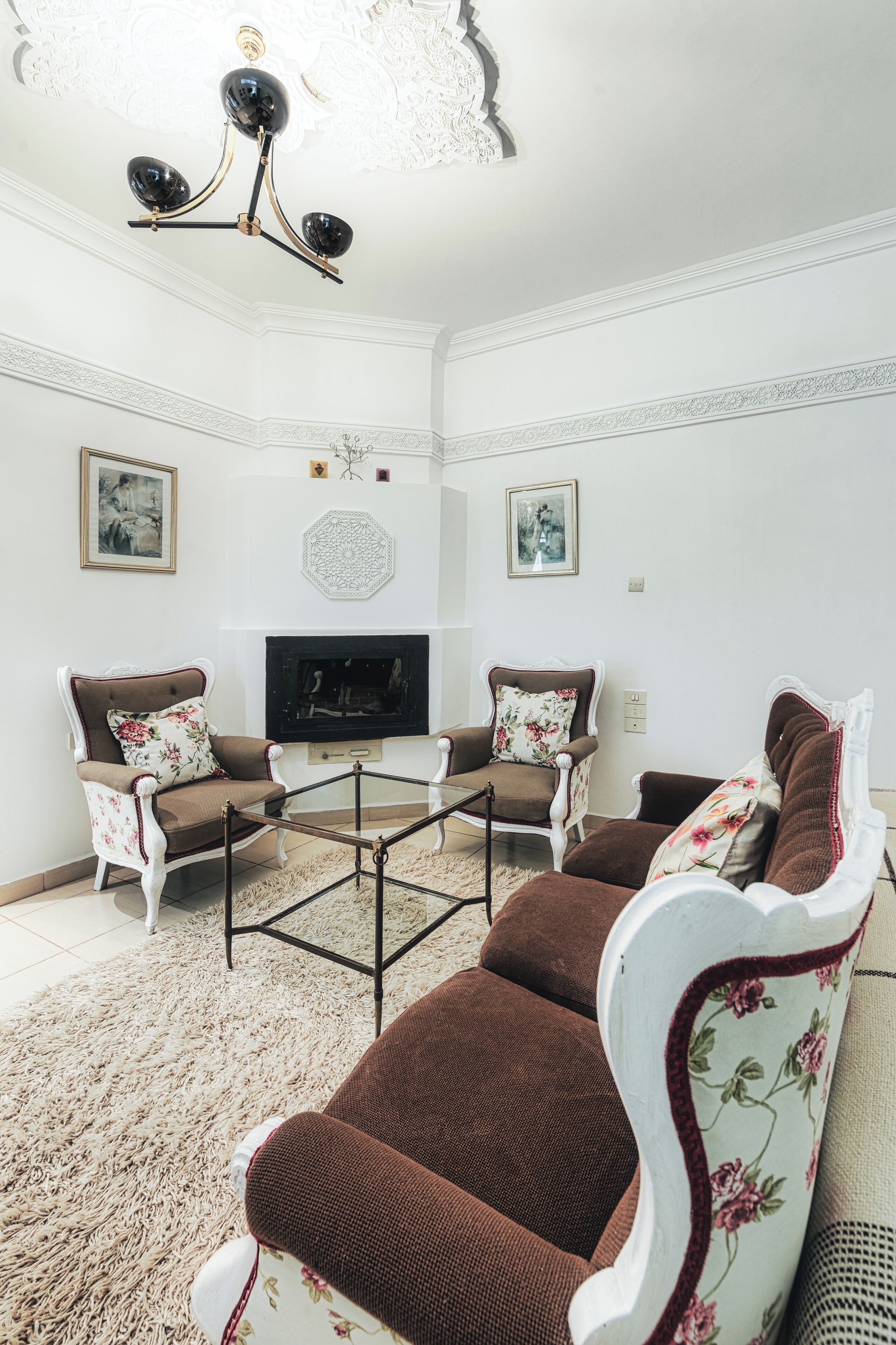 A living room with two armchairs, a glass coffee table, a fireplace, and a ceiling chandelier.