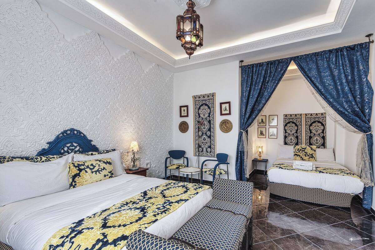 A bedroom with two beds, a patterned headboard, a decorative ceiling, and a nightstand with a lamp.
