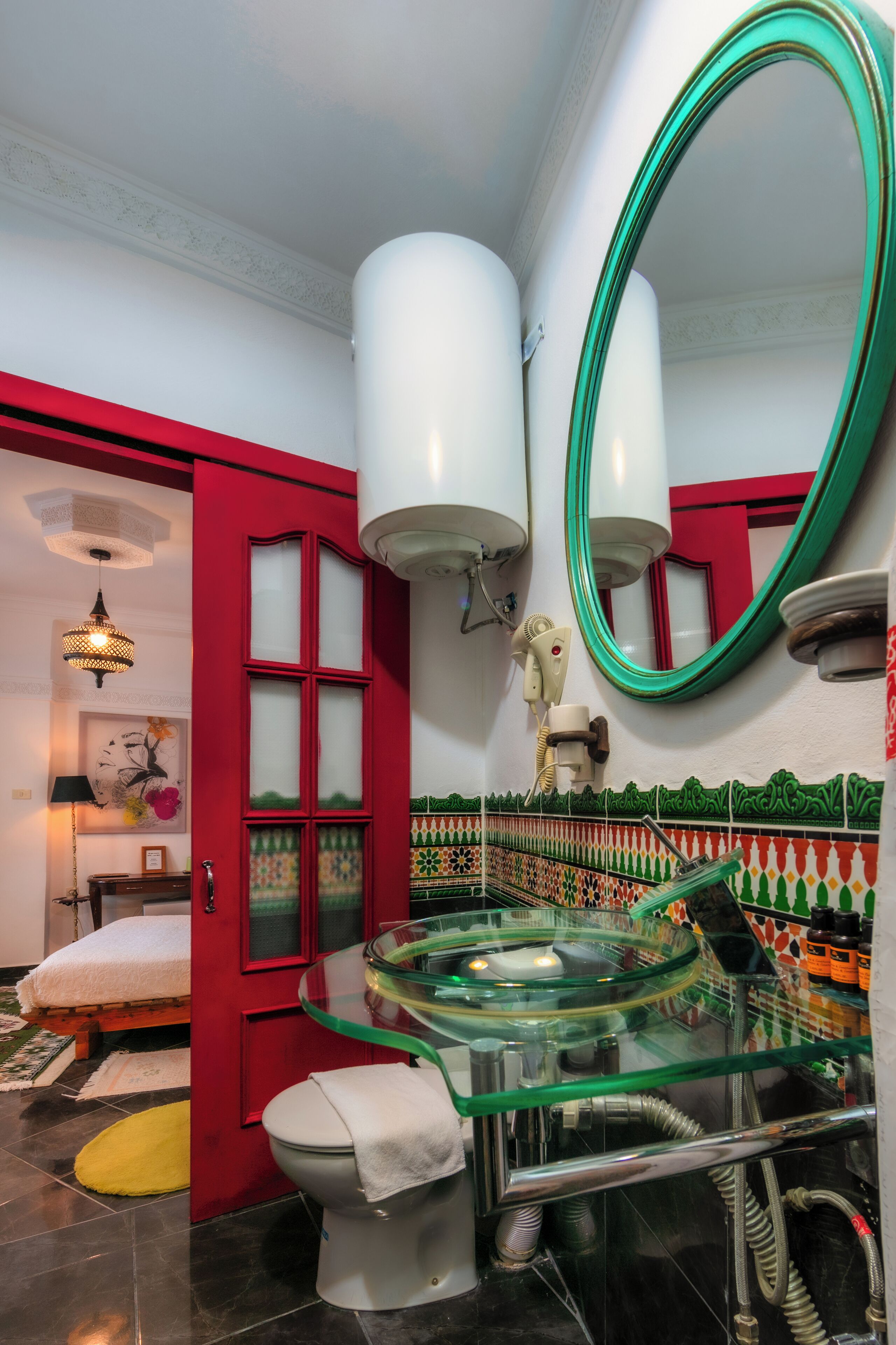 Un bagno con una porta rossa, un water bianco e un lavandino in vetro con uno specchio verde.