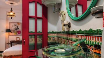 Un bagno con una porta rossa, un water bianco e un lavandino in vetro con uno specchio verde.