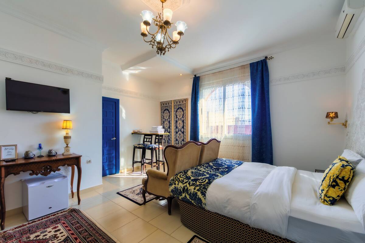 A hotel room with a bed, a desk, a chair, a television, and a chandelier.