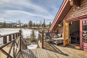 Une terrasse en bois avec des sièges d’extérieur, un chalet en bois à l’extérieur rouge et une montagne enneigée en arrière-plan.
