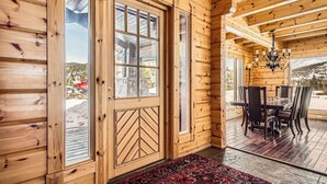 L’intérieur d’un chalet en bois, avec une grande porte, un coin repas avec des chaises et un lustre.