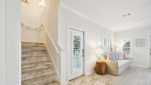 A staircase with white railings, a wooden door with glass panels, a beige sofa with a small wooden side table, and a patterned rug on a light-colored floor. - Community Pools | LSV | Close to Beach (Santa Rosa Beach)