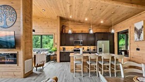 A spacious wooden cabin interior with a dining area, kitchen, and living room. - Stunning Cabin for 6 with Hot Tub & Pool Table! (Sevierville)