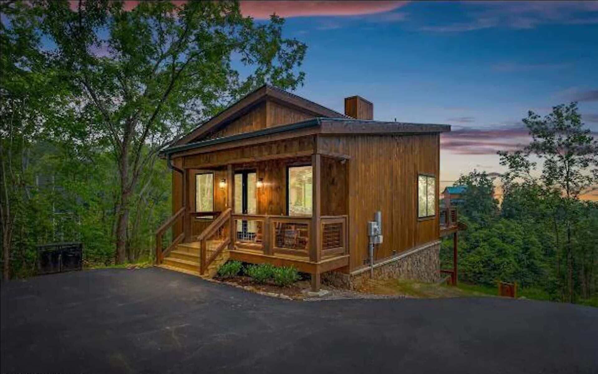 A wooden cabin with a porch, surrounded by trees.