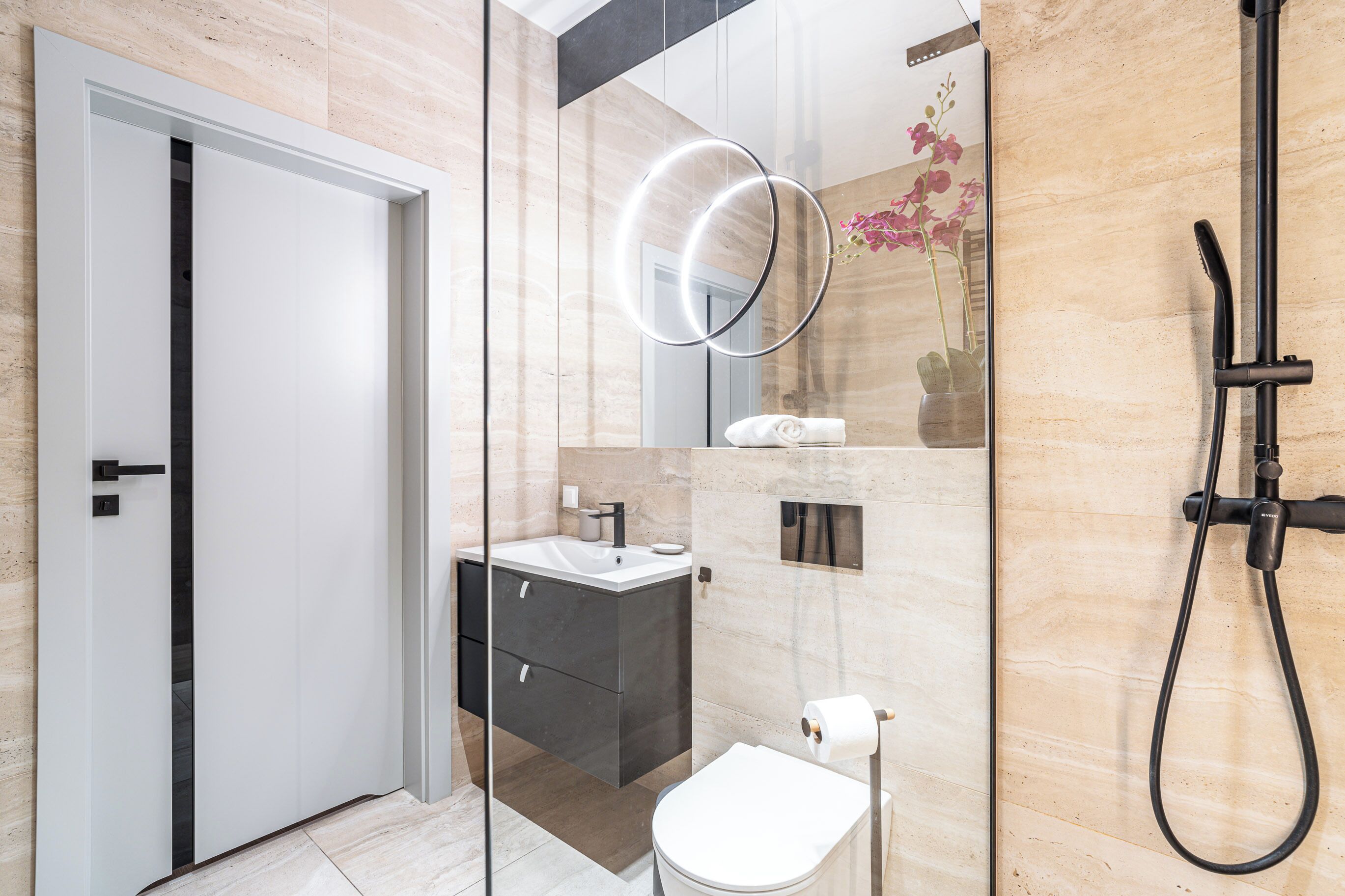 Un baño moderno con ducha de vidrio, inodoro blanco y tocador oscuro con espejo.