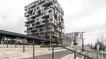 A modern multi-story building with balconies, a covered entrance, and a landscaped area with steps and railings.